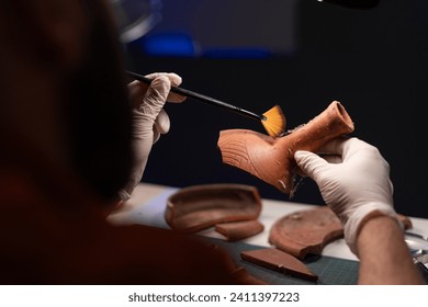 Archeologist studying and cleaning antique vessel while working late night in office. Archeological Digging. Close-up, trough shoulder view. Copy space - Powered by Shutterstock