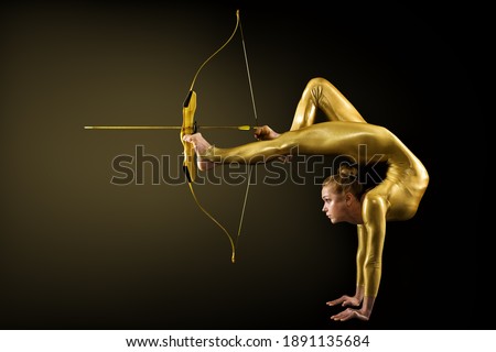 Archer Shooting by Legs with Gold Bow and Arrow. Flexible Gymnast aiming Target standing on Hand upside down. Goal Achievement Concept, Studio shot over Black background