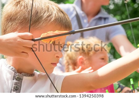 Archery junior championship. Summer sports. Summer holidays. Boy with green eyes pull the arrow. Kid stared at target. Child directed arrow at a target. Children and sports. Archery background