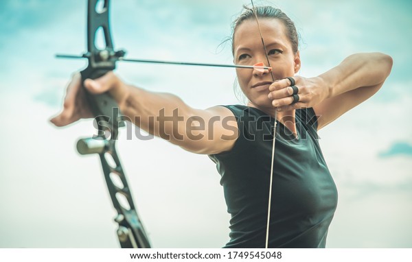 archery, young woman with an arrow in a bow\
focused on hitting a\
target