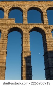 Arches of an ancient Roman aqueduct with the moon peeking out. Roman aqueduct of Segovia, Spain
