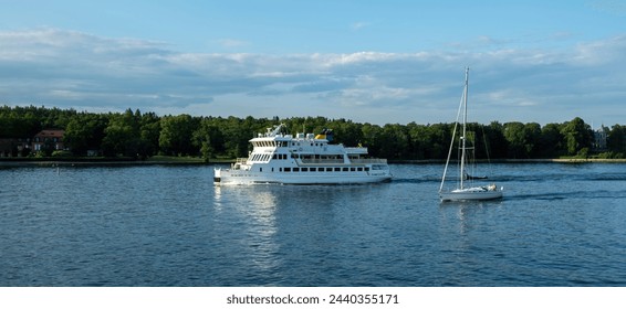 Archipelago Stockholm, cruise ship sails next to vessel in ripple sea water. Lush nature, traditional building, cloudy sky. Travel to Sweden. - Powered by Shutterstock