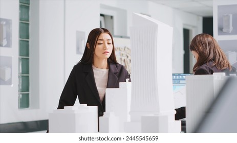 Architect analyzing blueprints and 3d building models at design table, trying to develop new industrial plan for residential area project. Woman measuring the dimensions and elements. - Powered by Shutterstock