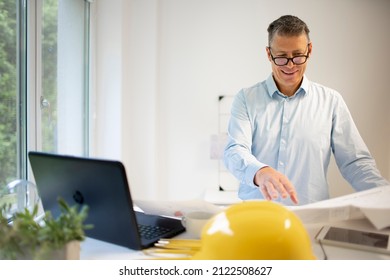 Architect with blue shirt is standing at height adjustable work table and is working