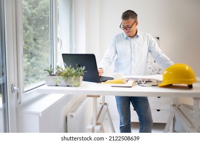 Architect with blue shirt is standing at height adjustable work table and is working