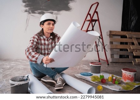 Architect builder studying layout plan of the rooms while sitting on the floor, serious civil engineer working with documents on construction site or home interior.Building, repair and home renovation