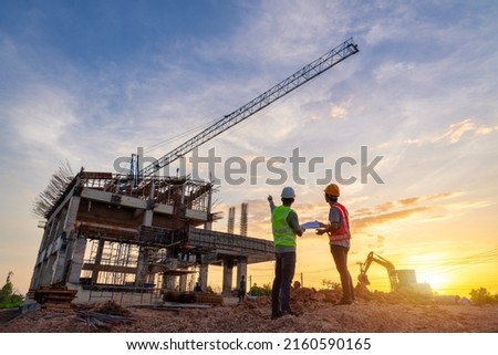 Architect civil Engineer and worker checking project at building site background, construction site at sunset in evening time. Silhouette of construction.
