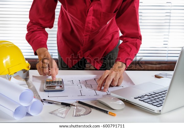 Architect concept. Architects man working with\
blueprints in the office.Architect hands using calculator measuring\
house blueprint.