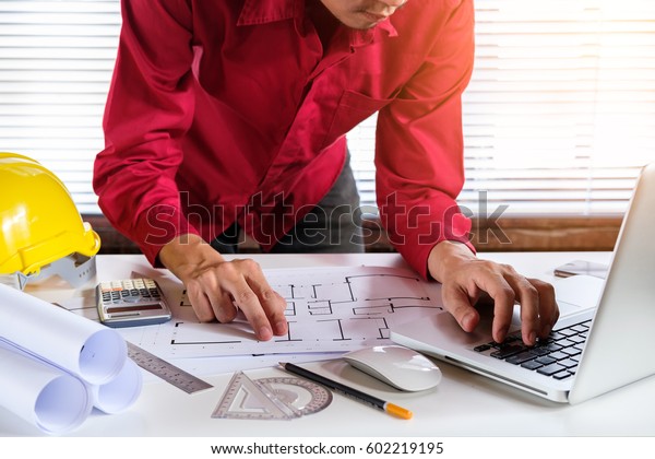 Architect concept. Architects man working with\
blueprints in the office.Architect hands working with laptop and\
house blueprint.