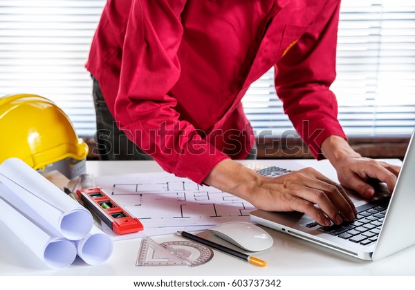 Architect concept. Architects man working with\
laptop computer in the office.Architect hands working with laptop\
and house blueprint.