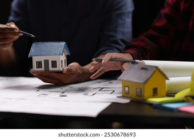 Architect discussing project using model house and blueprint. Architects discussing building plans with model house.