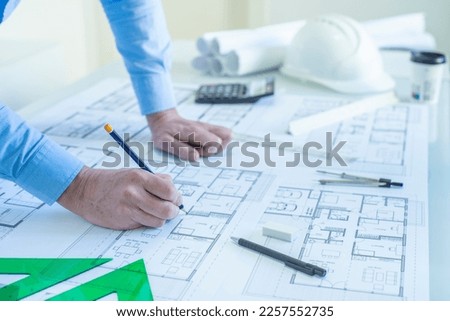 ARCHITECT OR DRAFTSMAN DRAWING PLANS OF THE FLOOR PROJECT OF A HOUSE ON THE DESK IN THE STUDIO. NEW HOMES PROMOTION CONCEPT.