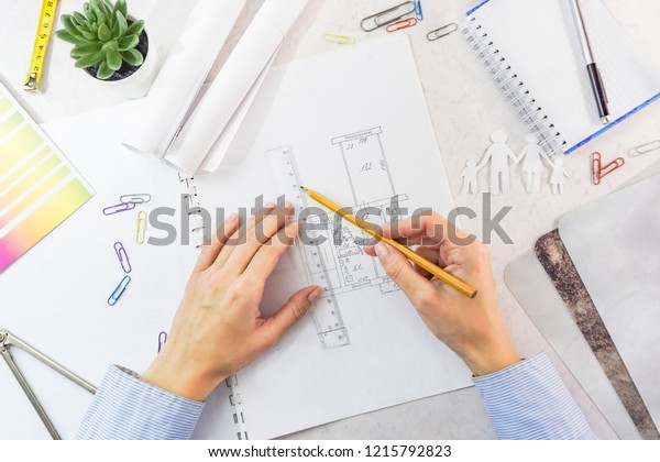 Architect drawing architectural project. Top view\
on unrecognizable designer hands working with building blueprint,\
copy space