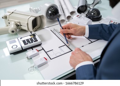 Architect Drawing Blueprint With Various Security Equipment On Desk