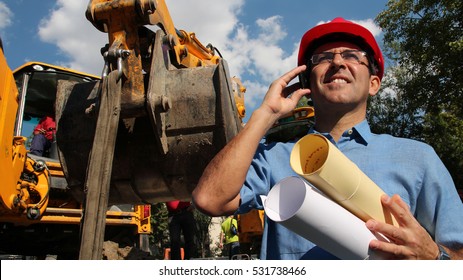 Architect or Engineer With Cell Phone on the Construction Site / Architect or Engineer holding blueprints and using cell phone at construction site