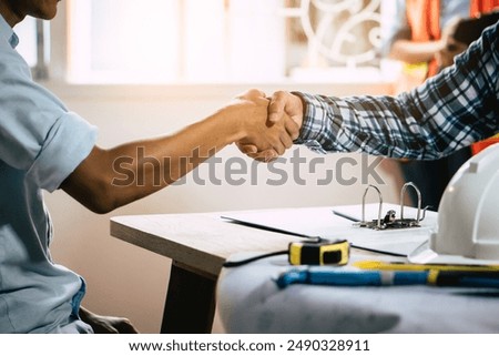 Architect and the engineer contractor shaking hands on building project, tools background.