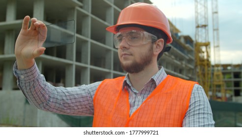 Architect or Engineer using smartphone transparent hologram digital display applicatiion in front of building under construction. Technology, people.