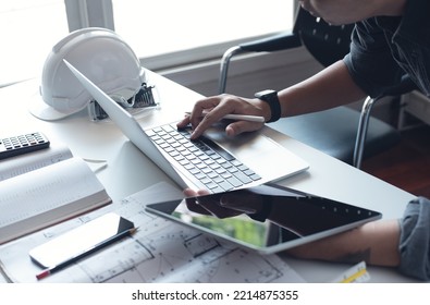 Architect or engineer working on laptop computer with blueprint, digital tablet and calculator on table in office at the construction site, close up	