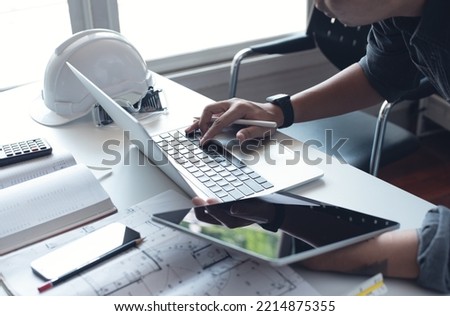 Architect or engineer working on laptop computer with blueprint, digital tablet and calculator on table in office at the construction site, close up	