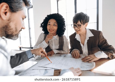 Architect explaining a project to two investors during a business meeting, fostering collaboration and discussing strategies in a bright office