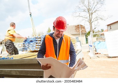 Architect Or Foreman Looks At A Blueprint With Building Material Delivery In The Background