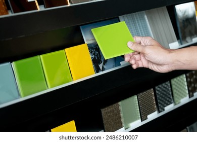 Architect hand choosing and picking green lacquered glass tile on material samples shelf display in the material library. Colorful acrylic sheet collection for interior finishing idea - Powered by Shutterstock