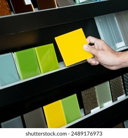 Architect hand choosing and picking yellow lacquered glass tile on material samples shelf display in the material library. Colorful acrylic sheet collection for interior finishing idea - Powered by Shutterstock