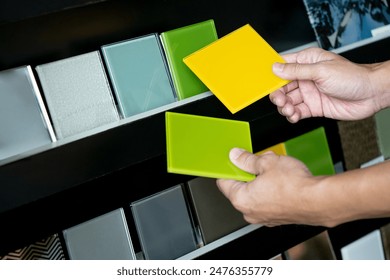 Architect hand compares yellow and green lacquered glass tiles from material samples shelf display in the material library. Colorful acrylic sheet collection for interior finishing idea - Powered by Shutterstock