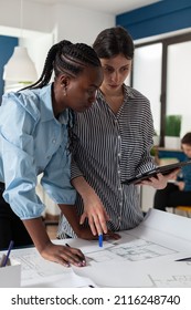 Architect Holding Digital Tablet Computer With Construction Plans Explaining Blueprints To African American Engineer Colleague. Professional Architects In Architectural Office Designing Urban