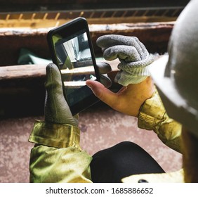 Architect holding a smartphone on construction site. young construction worker is using mobile phone on site. Construction worker with building plans and cellphone. Focus on mobile. warm vivid filter.