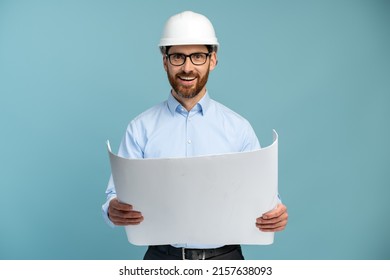 Architect man with cheerful face in builder safety helmet smiling while looking at the camera and holding blueprints over isolated background 