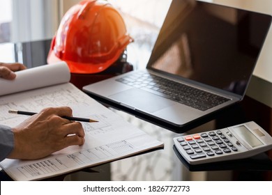 Architect man or male engineer hand hold pencil, writing and drawing architectural project, work on laptop computer with calculator on the desk at workplace. 