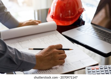 Architect man or male engineer hand hold pencil, writing and drawing architectural project, work on laptop computer with calculator on the desk at workplace.