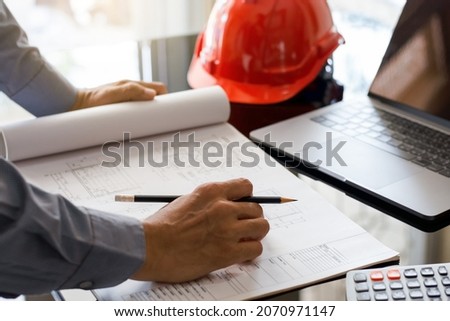 Architect man or male engineer hand hold pencil, writing and drawing architectural project, work on laptop computer with calculator on the desk at workplace.