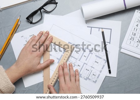 Architect with set square ruler working on project at grey table, top view