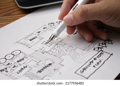 An architect sketching a residential building plan on white paper at a wooden table.