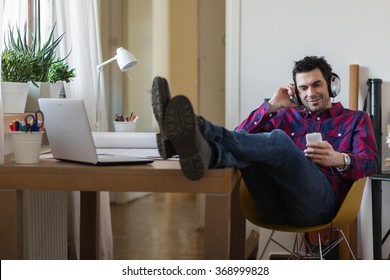 architect taking a break with his feet on the table, listening to music and browsing on his phone