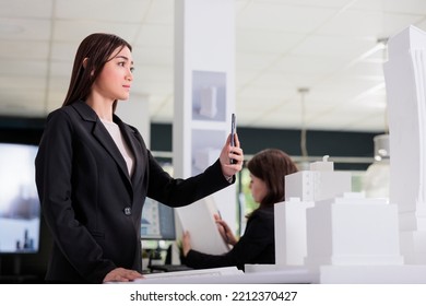 Architect Taking Building 3d Printed Model Photo On Smartphone, Real Estate Studio Employee Working With City Construction Project. Asian Worker Engineering In Architecture Coworking Space