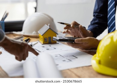 Architect using calculator with engineer reviewing blueprint for a tiny house project. Architect and engineer calculating cost and budget for building project, huddled over blueprint, discussing plan. - Powered by Shutterstock