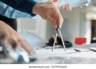 Architect using compass to design plans on a workspace table.