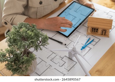 Architect using a digital tablet to design a sustainable and ecological house project with a small wind turbine, promoting renewable energy and green building practices - Powered by Shutterstock - Get 15% off with code: PIKWIZARD15