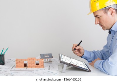 Architect using digital tablet on office table desk. Model house construction with brick on blueprint