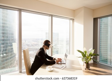 Architect using innovative VR headset for work with 3d visualization. Man at desk working on laptop in virtual reality glasses on head. Modern digital office, augmented and advanced virtual workspace