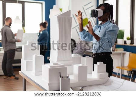 Architect using vr headest to look at white foam scale model of real estate project. Engineer working with augmented reality looking at table with skyscraper building maquette.