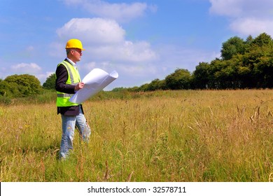 Architect wearing site safety gear and holding plans surveying a new building plot