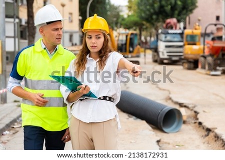 Architect woman talking with master builder about construction project in constriction site. Woman pointing with finger on something. Foto d'archivio © 
