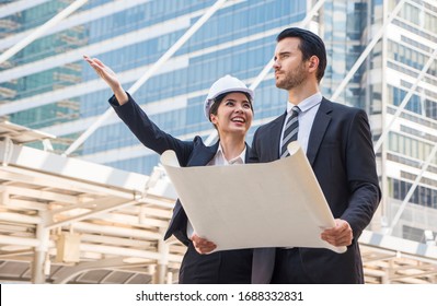 ฺBeautiful Architect Wore A Suit And Helmet, Standing And Talking To A Male Businessman In A Real Estate Construction Project.Estate Property Development Concept.
