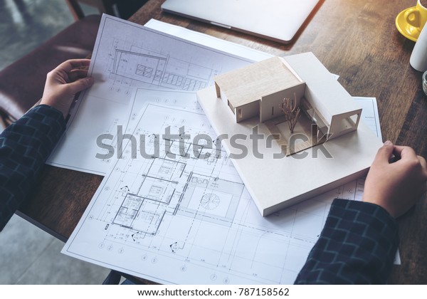 An architect working and looking\
at an architecture model with shop drawing paper on\
table