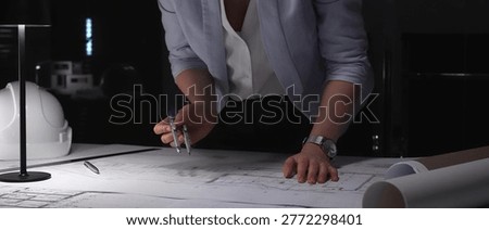 Architect working at night, drafting blueprints with a compass, planning urban construction projects.