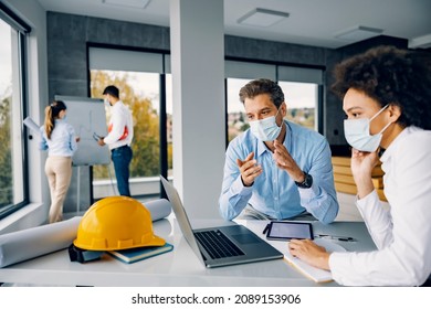 Architect working in an office during covid. Multicultural architects are sitting in the office with a mask on their faces, looking at the laptop and working on the project. - Powered by Shutterstock